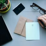 Overhead view of a desk with writing tools, glasses, envelope, and notebooks, showcasing office work essentials.