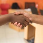 Two women exchanging a handshake in a professional indoor office setting.